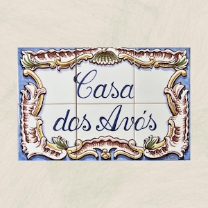 Könnte beinhalten: Dekorative Fliesentafel mit dem Text "Casa dos Avós" in eleganter blauer Schrift. Die weißen Fliesen sind von einem blauen Rand und aufwendigen, farbenfrohen Verzierungen in Gold, Braun und Grün umrahmt.