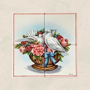 Pode incluir: Duas pombas brancas empoleiradas em uma cesta tecida cheia de flores rosa, vermelhas e azuis. As pombas estão uma de frente para a outra e a cesta está sobre uma superfície branca. A imagem é assinada "F. Gianna".