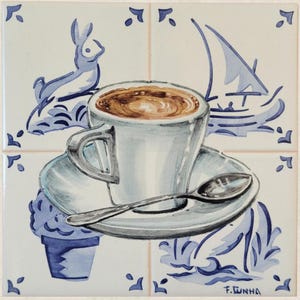 Pode incluir: Azulejo de cerâmica pintado à mão com uma chávena de café num pires com uma colher. O design inclui ilustrações náuticas em azul e branco de um veleiro, um coelho e detalhes florais. O azulejo é quadrado.