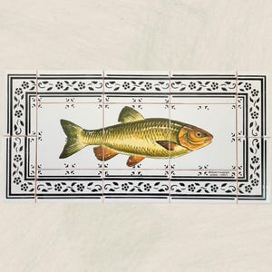 May include: A rectangular tile set featuring a hand-painted fish in shades of gold, brown, and orange. The fish is centered on a white background, framed by a black border with floral and geometric patterns. The tile set is suitable for kitchen or bathroom decor.