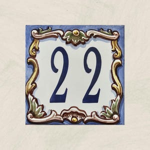 May include: A blue and white ceramic tile with a gold and green decorative border. The tile features the number 22 in blue.