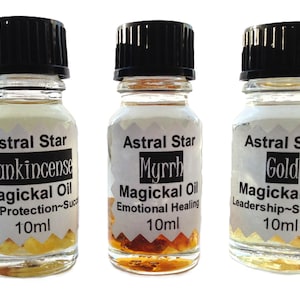 May include: Three small glass bottles with black caps, each containing a different essential oil. The bottles are labeled "Astral Star Frankincense Magickal Oil Healing~Protection~Success 10ml", "Astral Star Myrrh Magickal Oil Emotional Healing 10ml", and "Astral Star Gold Magickal Oil Leadership~Strength 10ml".