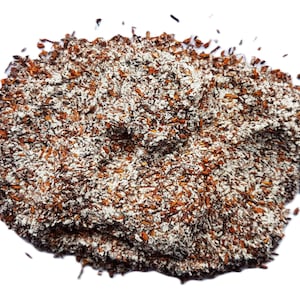 May include: A pile of brown and white textured material, possibly a spice or food product, against a white background. The material appears to be granular with a mix of colors and textures.