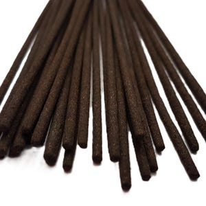 Puede incluir: Un manojo de varitas de incienso finas de color marrón oscuro dispuestas en forma de abanico. Cada varita tiene una superficie texturizada y granulada con una forma cilíndrica uniforme que se estrecha ligeramente hacia los extremos.