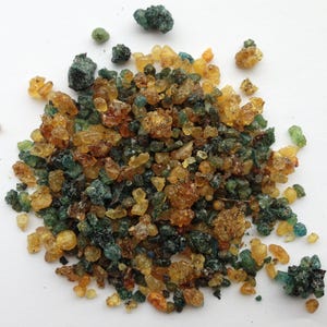 May include: A close-up of a pile of small, irregularly shaped pieces of resin. The resin is a mix of green, brown, and yellow colors.