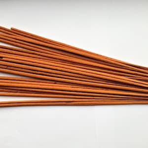 May include: A bundle of brown incense sticks arranged in a fan shape on a white surface.
