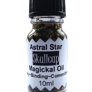 Könnte beinhalten: Kleine Glasflasche mit schwarzem Verschluss, gefüllt mit grüner Flüssigkeit und Kräutern. Das Etikett trägt die Aufschrift "Astral Star Skullcap Magickal Oil" und "10ml". Die Flasche ist für spirituelle Praktiken bestimmt.