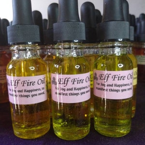 May include: Three glass bottles with black dropper tops filled with a yellow liquid. Each bottle has a pink label with the text "Elf Fire Oil" and a description of the oil's purpose. The bottles are arranged in a row on a purple surface.
