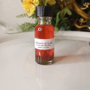 May include: A small, clear glass bottle with a black cap filled with a red liquid and gold glitter. The label reads "Showers of Gold" and "For use when long term wealth is desired."