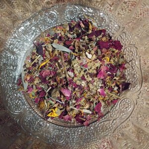 May include: A glass bowl filled with a mixture of dried herbs, flowers, and petals. The mixture includes dried rose petals, lavender, and other herbs. The bowl is decorated with a floral pattern.