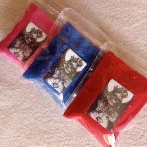 May include: Three small pouches made of felt in pink, blue, and red. Each pouch has a clear plastic window showing a black and white image of a woman with a crown and flowers.