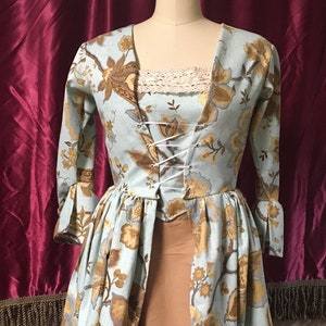 May include: A light blue and brown floral print dress with a white lace bodice and a brown skirt. The dress has a fitted bodice with a lace-up front and a flowing skirt.