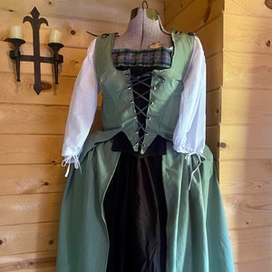 May include: A green and black renaissance style dress with a lace-up bodice and a long skirt. The dress is on a mannequin and has a plaid fabric detail on the bodice.