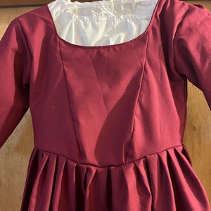 May include: A maroon dress with a white gathered neckline and long sleeves. The dress has a fitted bodice and a full skirt with pleats.
