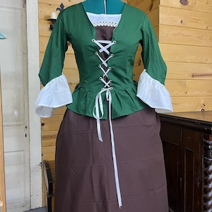 May include: A green and brown dress with a white lace neckline and white lace trim on the sleeves. The dress has a lace-up bodice and a brown skirt.