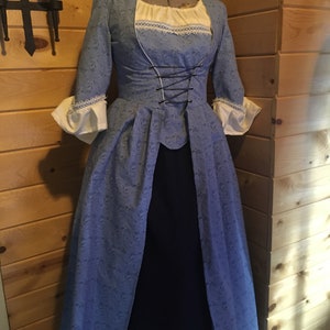 May include: A blue and white dress with a lace trim and a black ribbon corset. The dress has a fitted bodice and a full skirt.