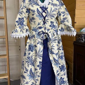 May include: A long white dress with a blue floral pattern and a lace trim. The dress has a lace-up bodice and a blue skirt.