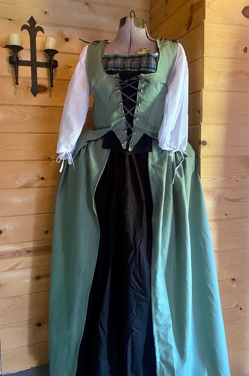May include: A green and black renaissance style dress with a lace-up bodice and a long skirt. The dress is on a mannequin and has a plaid fabric detail on the bodice.