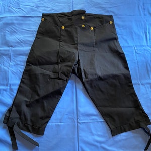 Puede incluir: Pantalón de algodón negro de cintura alta con cierre de botón. El pantalón tiene pierna ancha y está atado en la parte inferior con correas negras.