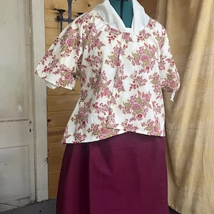 May include: A white blouse with a floral print and a burgundy skirt. The blouse has a white collar and short sleeves. The skirt is long and flowy.