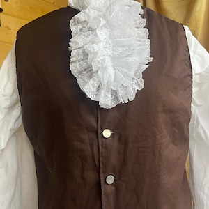以下が含まれることがあります： 3つの銀色のボタンと白いレースのフリル襟が付いた茶色のベスト