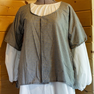 May include: A white dress with a black and white gingham top layer. The dress has a round neckline and short sleeves.