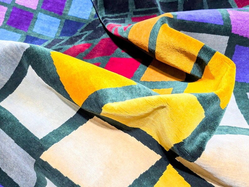 Puede incluir: Una alfombra colorida con patrones geom&eacute;tricos con una variedad de formas y colores. La alfombra presenta cuadrados, tri&aacute;ngulos y rombos en tonos de amarillo, morado, azul, rojo y gris. Los bordes est&aacute;n delineados en verde oscuro.