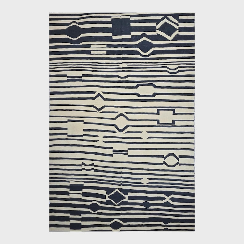 Pu&ograve; includere: Un tappeto rettangolare con sfondo color crema e un motivo a strisce orizzontali blu navy. Le strisce sono interrotte da varie forme geometriche, tra cui diamanti, quadrati e rettangoli. Il tappeto ha un design moderno e astratto.