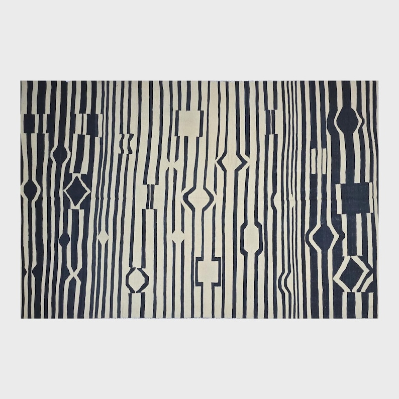 Pu&ograve; includere: Un tappeto rettangolare con sfondo color crema e strisce verticali blu navy. Le strisce sono intervallate da forme geometriche, tra cui quadrati, diamanti e ovali allungati. Il tappeto ha un design moderno e astratto.