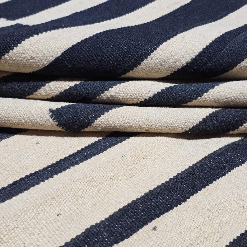 Pu&ograve; includere: Tappeto piegato con strisce blu navy e bianco sporco alternate. Il tappeto &egrave; realizzato in un materiale strutturato, con le strisce diagonali. Il tappeto &egrave; piegato, mostrando pi&ugrave; strati del motivo a strisce.