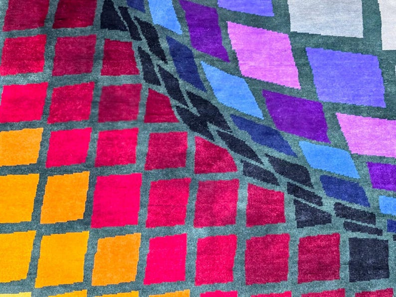 Puede incluir: Una colorida alfombra con un dise&ntilde;o geom&eacute;trico. El dise&ntilde;o presenta una cuadr&iacute;cula de formas de rombos en tonos de rojo, naranja, rosa, morado, azul y negro sobre un fondo gris. La alfombra tiene una apariencia texturizada.