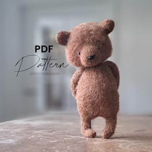 May include: A handmade brown teddy bear with a textured, knitted appearance. The bear has small, round ears, a black nose, and is standing with its hands behind its back. The image includes the text "PDF Pattern" and the Instagram handle "@sosole.puppen".