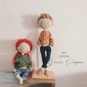 Könnte beinhalten: Zwei handgefertigte Häkelpuppen, eine mit roten Haaren und einem grünen Pullover, die andere mit braunen Haaren und einem orangefarbenen Pullover. Beide Puppen tragen blaue Jeans. Der Text "PDF E-BOOK Sosole Puppen" ist sichtbar.