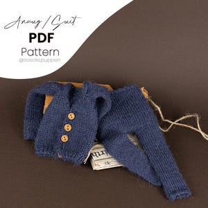 Puede incluir: Un traje de punto azul para bebé con tres botones marrones en la parte delantera. El traje está colocado sobre una superficie marrón con un trozo de papel debajo. El texto "Anzug / Suit PDF Pattern @sosole.puppen" es visible en la esquina superior izquierda de la imagen.