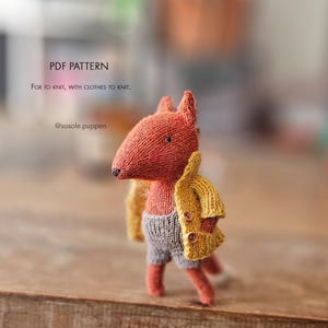 May include: A small knitted fox toy wearing a yellow cardigan with two brown buttons and grey shorts. The text PDF PATTERN Fox to knit, with clothes to knit. @sosole.puppen is visible in the upper left corner of the image.