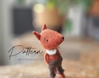 PDF knitting pattern for a fox with clothes. Includes a skirt, pants, coat, and collar. Languages: German, English
