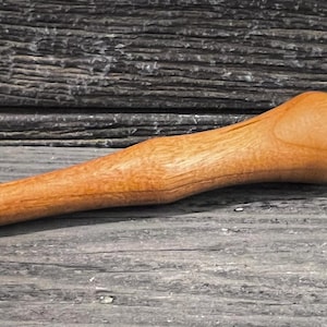 May include: A wooden mallet with a long handle and a rounded head. The head is light brown with a white and black band around the striking surface. The mallet is made of light-coloured wood.