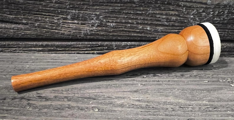 May include: A wooden mallet with a long handle and a rounded head. The head is light brown with a white and black band around the striking surface. The mallet is made of light-coloured wood.
