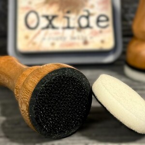 May include: A wooden handled ink blending tool with a black foam applicator, a separate white foam applicator, and a stamp pad with the word "Oxide" visible. The tools are for crafting and scrapbooking.