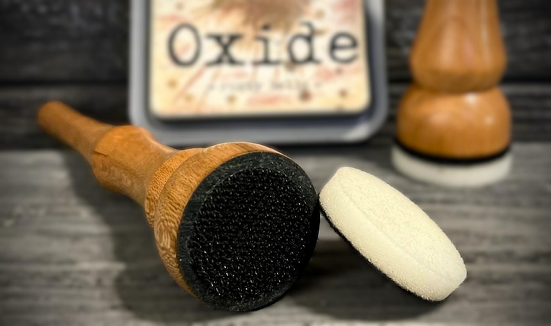May include: A wooden handled ink blending tool with a black foam applicator, a separate white foam applicator, and a stamp pad with the word "Oxide" visible. The tools are for crafting and scrapbooking.