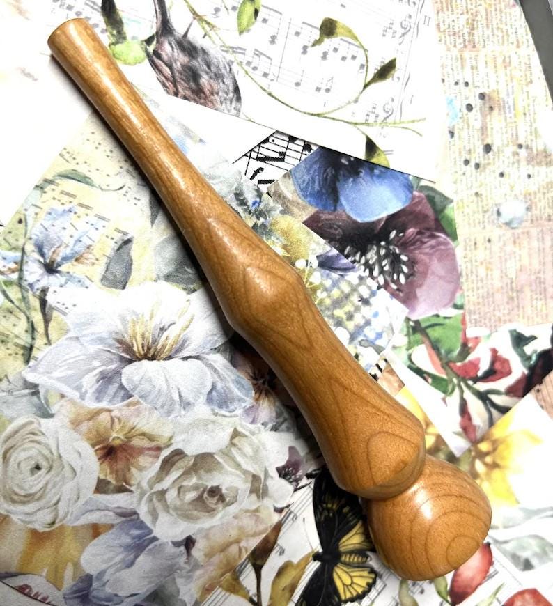May include: A light brown wooden rolling pin. The handle is long and cylindrical, with a bulbous end. The rolling pin is made of light-coloured wood and is designed for rolling out dough. The rolling pin measures approximately 30 cm in length.