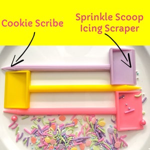 May include: Three cookie decorating tools: a purple cookie scribe, a yellow cookie scribe, and a pink sprinkle scoop icing scraper. The tools are on a white surface with colorful sprinkles.