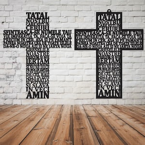 Puede incluir: Una cruz de madera negra con la oración del Señor escrita en rumano. La cruz está montada en una pared de ladrillo blanco.