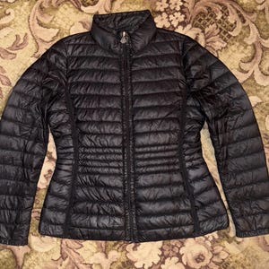 Puede incluir: Chaqueta acolchada negra con cierre de cremallera y cuello alto.