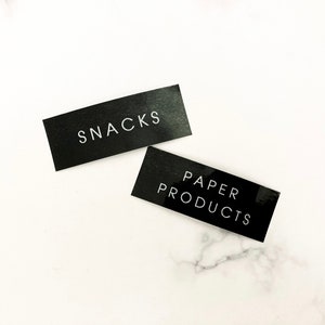 May include: Two black rectangular labels with white text. The top label says "SNACKS" and the bottom label says "PAPER PRODUCTS".
