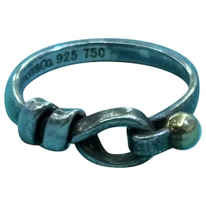 May include: A sterling silver ring featuring a knot-like design with a small gold-toned sphere at one end. The interior of the band is engraved with the text Tiffany & Co 925 750, indicating a combination of silver and gold metal materials.