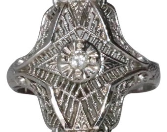 May include: A silver filigree ring with a small, round diamond in the center.