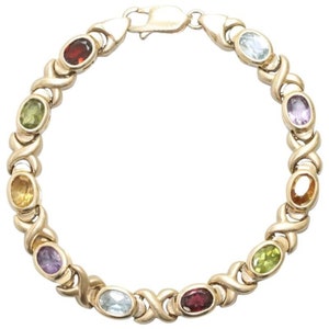 May include: A gold bracelet with a delicate, interwoven design. It features a series of oval-shaped gemstones in various colors, including green, yellow, blue, purple, and red.