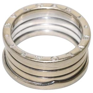 May include: A silver-toned metal ring featuring a multi-band design with a central coiled structure. The top and bottom edges of the ring are engraved with the text BVLGARI, repeating around the circumference of the polished metallic surface.