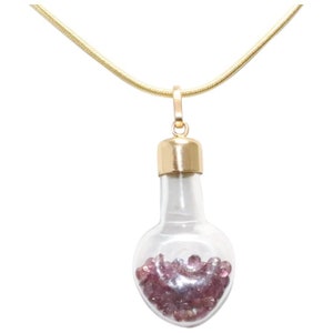 May include: A gold chain necklace with a pendant shaped like a glass bottle filled with small pink gemstones.